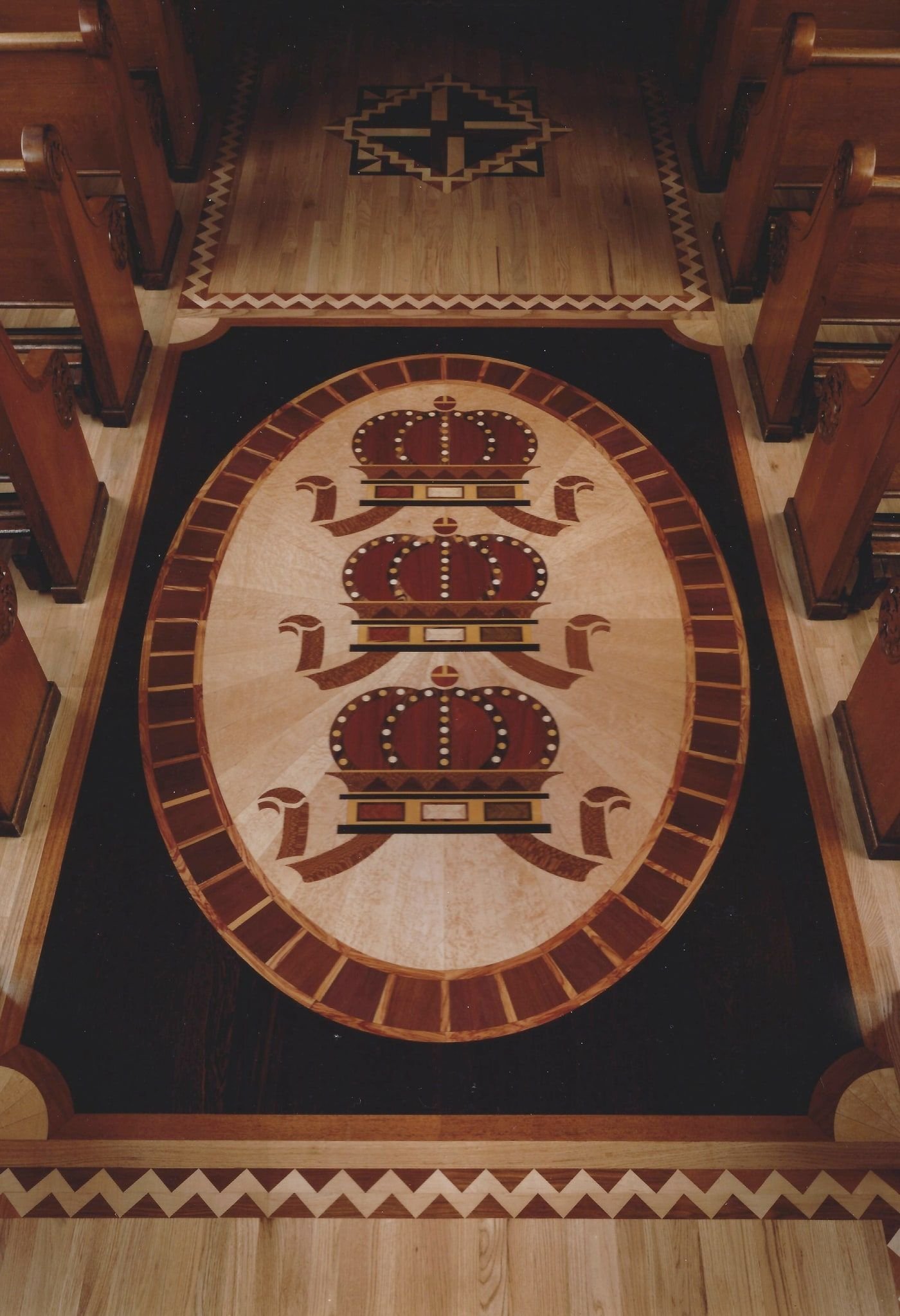Oval medallion of three inlaid crowns on a radiating field, ringed and set into a dark border — Church of St. John Cantius, Chicago, 1998