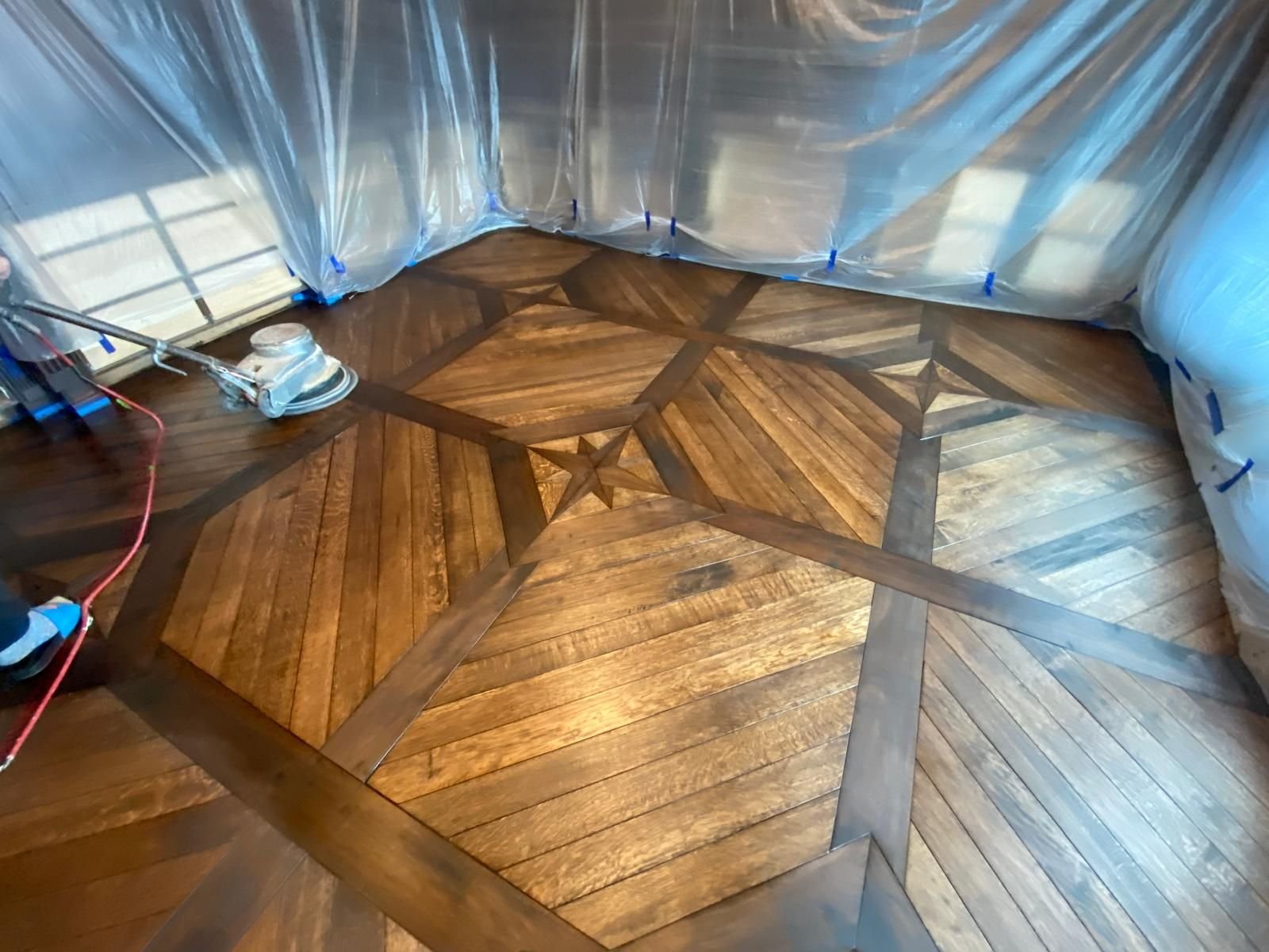 Star parquetry field being sanded under plastic sheeting, border and star already laid — custom commission