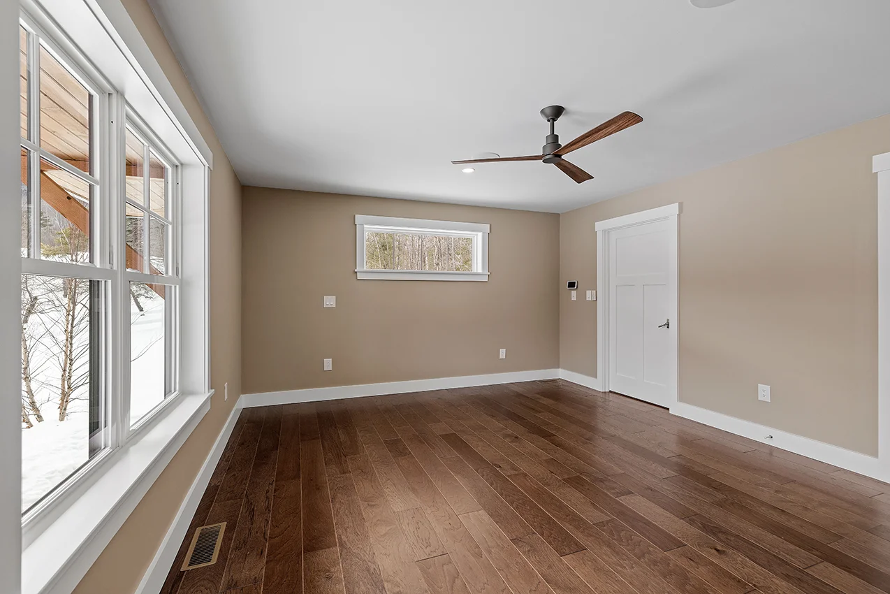 Large empty room with a ceiling fan over a warm, freshly restored wood floor