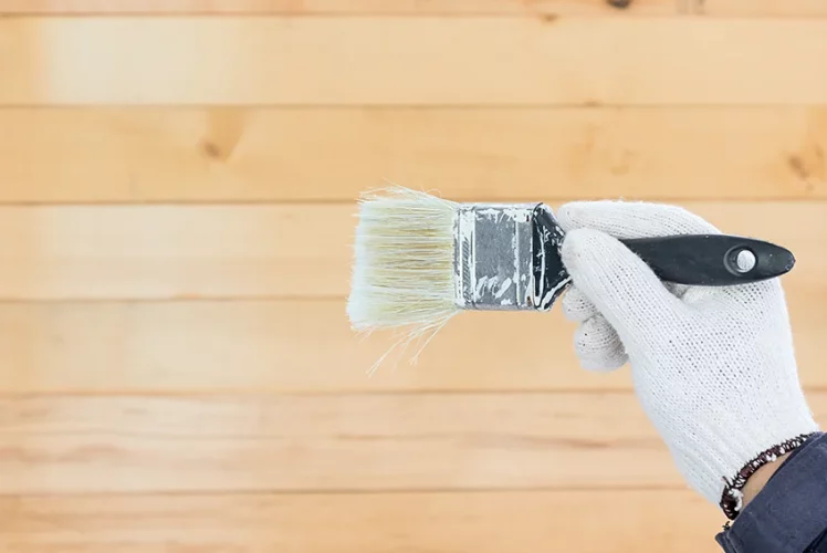 Gloved hand holding a brush over stain