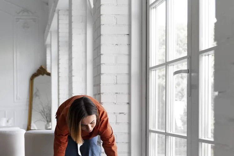 Person standing in a bright, newly floored room beside a tall window